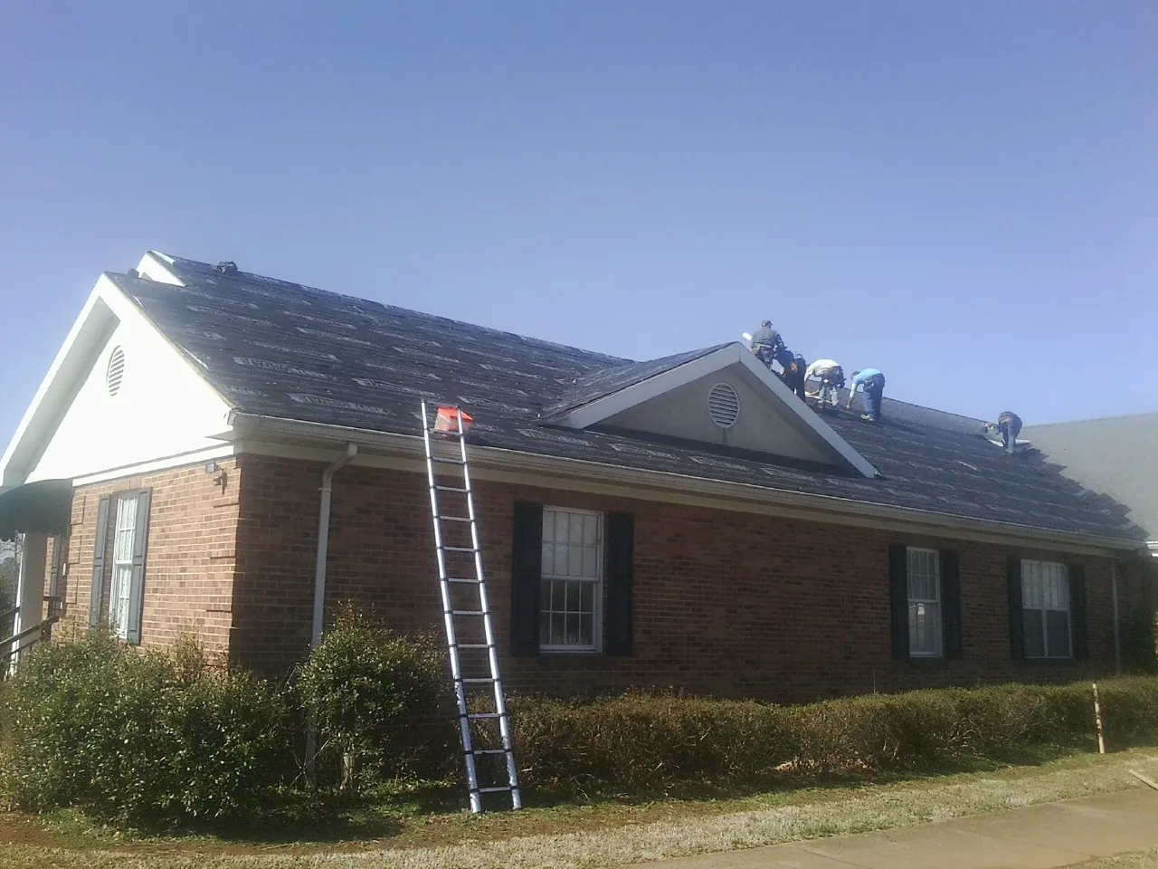 Crew tearing shingles off a brick ranch roof with a ladder set — Emergency Roof Repair work by our crew in Mc Henry