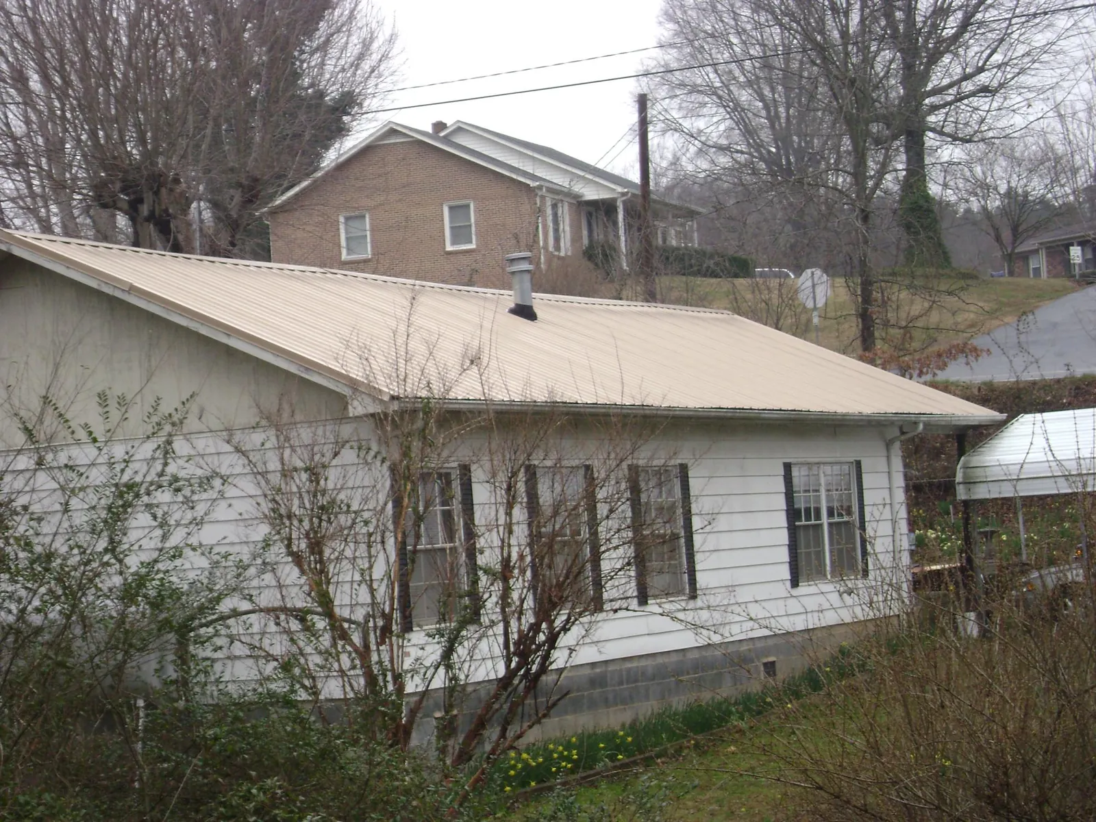 Tan metal roof on a white sided house set into a hillside in Mc Henry